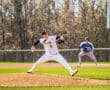 A baseball pitcher in a striped uniform throws a pitch on a sunny day, while a batter waits in the background.