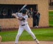 A baseball player in a striped uniform prepares to swing at a pitch during a game, with fans in the background.