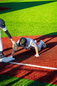 A baseball player hand slides into base while another player reaches for him, showcasing an intense moment on the field.