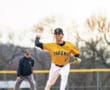 High school pitcher in a yellow Tigers uniform throws a baseball on the mound, with an umpire in the background.