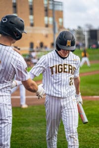 Baseball players in striped uniforms shake hands on the field, celebrating a play during a game.