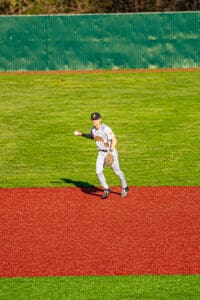 A baseball player in a gray uniform catches a ball on a vibrant red field, ready to make a play.