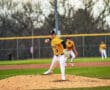 Baseball pitcher in action on the mound, wearing a yellow jersey and focused on delivering a pitch at a game.