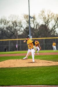 Baseball pitcher in action on the mound, wearing a yellow jersey and focused on delivering a pitch at a game.