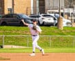 Baseball player in a striped uniform throws a ball from the infield during a sunny game day on the field.