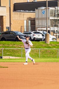 Baseball player in a striped uniform throws a ball from the infield during a sunny game day on the field.