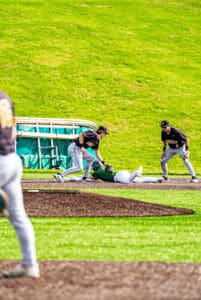 Baseball players in action during a game, with one player sliding into base while teammates prepare to make a play.