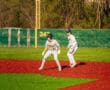 Baseball players on vibrant turf, one leading off base while the other prepares for a play in a sunny outdoor setting.