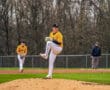 Baseball pitcher on the mound in a yellow team jersey, preparing to throw during a game, with teammates in the background.