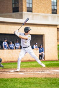 Baseball player swings bat at the pitch, wearing a black helmet and striped uniform, with teammates in the background.