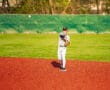 Young baseball player in a gray uniform fields a ball on a vibrant red baseball diamond during a sunny day.