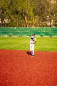 Young baseball player in a gray uniform fields a ball on a vibrant red baseball diamond during a sunny day.