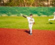 Young baseball player in a Tigers uniform preparing to throw a ball on a vibrant red field during practice.