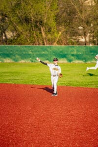 Young baseball player in a Tigers uniform preparing to throw a ball on a vibrant red field during practice.