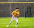 High school baseball player in yellow jersey fielding on the grass during a game. Athletic action shot with motion.