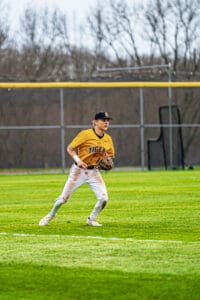 High school baseball player in yellow jersey fielding on the grass during a game. Athletic action shot with motion.
