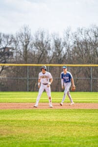 Two high school baseball players on the field, one on second base, in a sunny spring game.