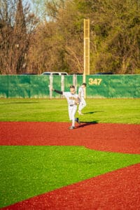 Young baseball player in Tigers uniform throws a ball on a vibrant, colored field during a game.