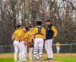 A baseball team gathers on the mound for a strategy discussion during a game, wearing yellow and black uniforms.