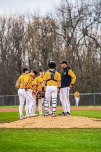 A baseball team gathers on the mound for a strategy discussion during a game, wearing yellow and black uniforms.