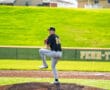 Baseball pitcher in action, balancing on the mound under a sunny sky, preparing to throw a pitch in a game.