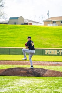 Baseball pitcher in action, balancing on the mound under a sunny sky, preparing to throw a pitch in a game.