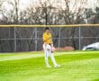 Baseball player in a yellow jersey stands in the outfield, ready for action on a sunny day. Lush green grass surrounds him.