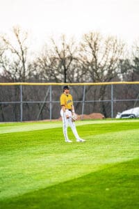 Baseball player in a yellow jersey stands in the outfield, ready for action on a sunny day. Lush green grass surrounds him.