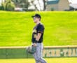 Baseball player in black jersey stands on field, wearing sunglasses and holding glove, ready for the game.