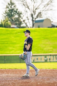 Baseball player in black jersey stands on field, wearing sunglasses and holding glove, ready for the game.