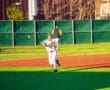 A player in a baseball uniform throws a ball while running on a bright green field during a game.