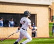 Baseball player swings bat during a game, showcasing athleticism on the field in a sunny setting.