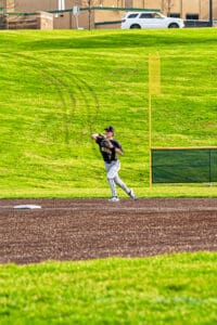 Baseball player in action, throwing a ball on a sunny day at the field, with green grass and dirt in the background.