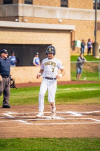 Baseball player in pinstripes crossing home plate, umpire in the background, vibrant field setting.