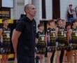 Basketball coach stands confidently with players during team lineup, showcasing unity before a game.