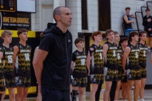 Basketball coach stands confidently with players during team lineup, showcasing unity before a game.