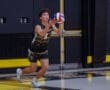 Young male volleyball player prepares to serve with a colorful volleyball in a gym setting, showcasing athleticism and focus.