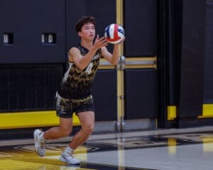 Young male volleyball player prepares to serve with a colorful volleyball in a gym setting, showcasing athleticism and focus.