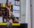 A volleyball player prepares to serve, captured in action during a competitive match with a scoreboard in the background.