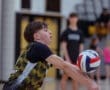 A young volleyball player dives to receive the ball during a dynamic game at a gymnasium.