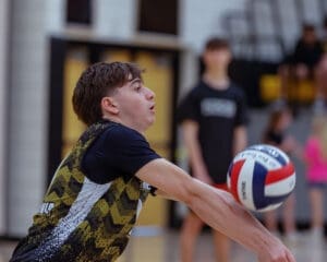 A young volleyball player dives to receive the ball during a dynamic game at a gymnasium.