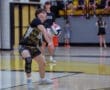 A volleyball player in action, receiving a serve with intense focus during a gymnasium practice session.