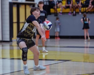 A volleyball player in action, receiving a serve with intense focus during a gymnasium practice session.