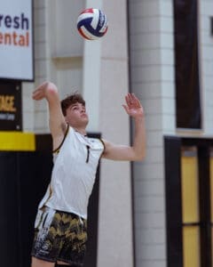 Teenage volleyball player serves the ball in a gym, showcasing focus and athleticism in a dynamic moment.