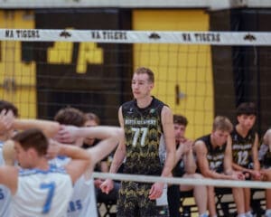 North Allegheny volleyball player #77 stands focused during a game, with teammates in the background near the net.