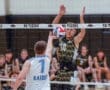 Volleyball player attempts a block at the net while an opposing player prepares to spike the ball.