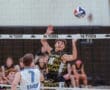 High school volleyball match: player #14 jumps to spike the ball over the net against a rival team, showcasing athletic skill.