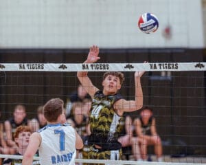 High school volleyball match: player #14 jumps to spike the ball over the net against a rival team, showcasing athletic skill.