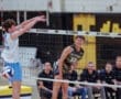 High school boys' volleyball match: player spikes ball over the net while teammate prepares for defense in a competitive atmosphere.