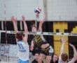 High school volleyball game action; player spikes ball over the net while opposing team attempts to block.